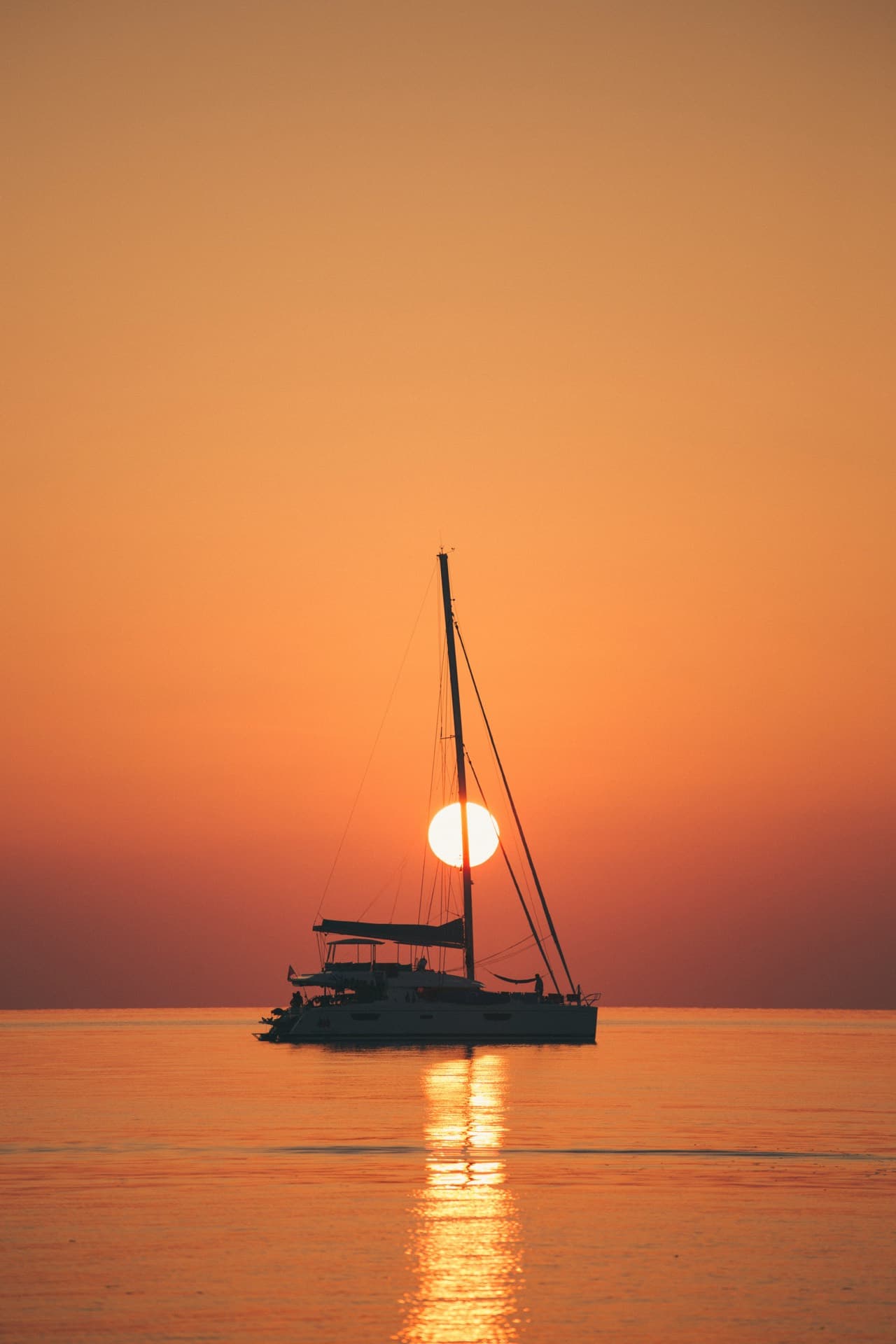 A yacht silhouetted against the setting sun on a calm, empty sea
