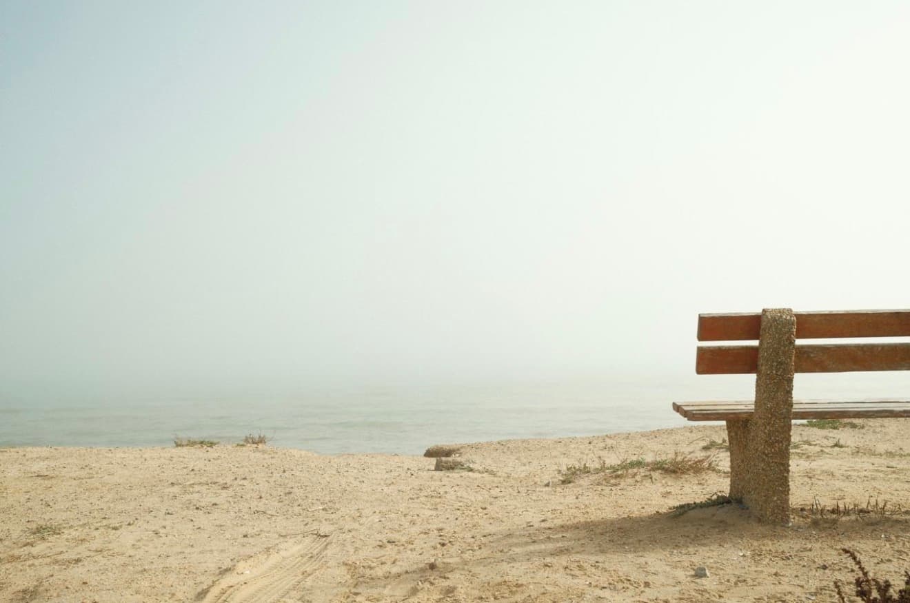 An empty bench overlooking a hazy, quiet sea