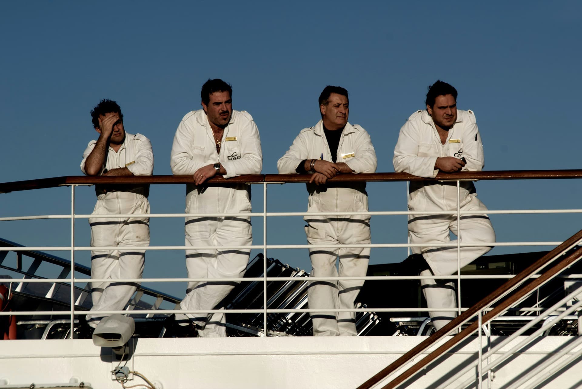 Four crew in uniform leaning on a ship's rail, one looking weary