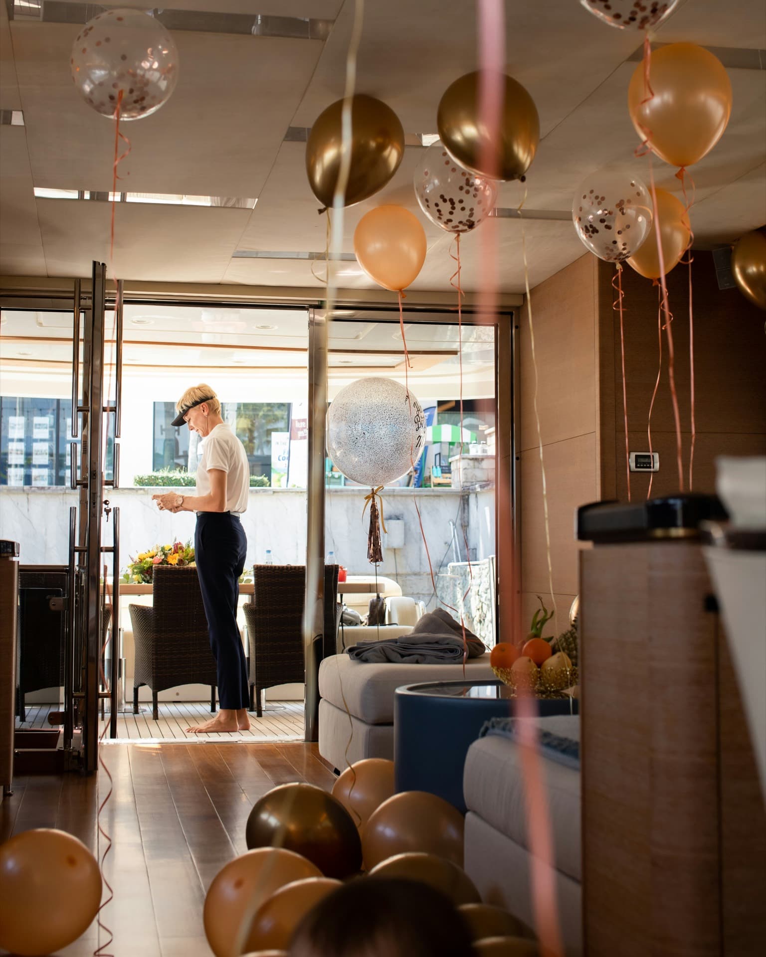 A yacht crew member standing alone with their phone amid party balloons in a saloon